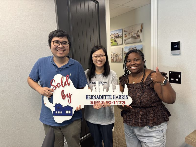 Bernadette Harris with two clients and her Sold key sign at a builder sales office
