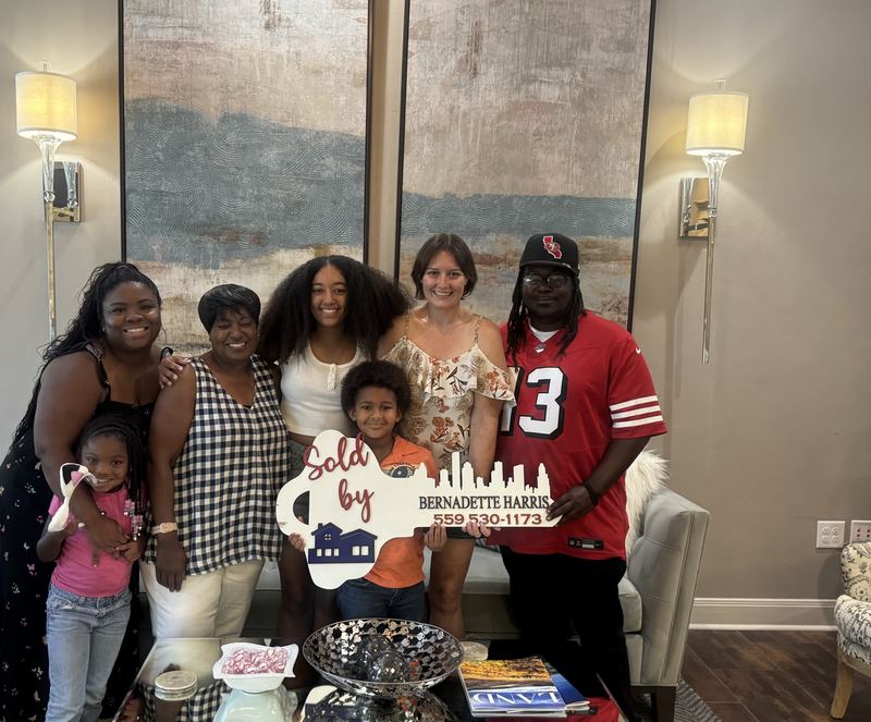 Bernadette Harris with a family of clients holding her Sold key sign on closing day